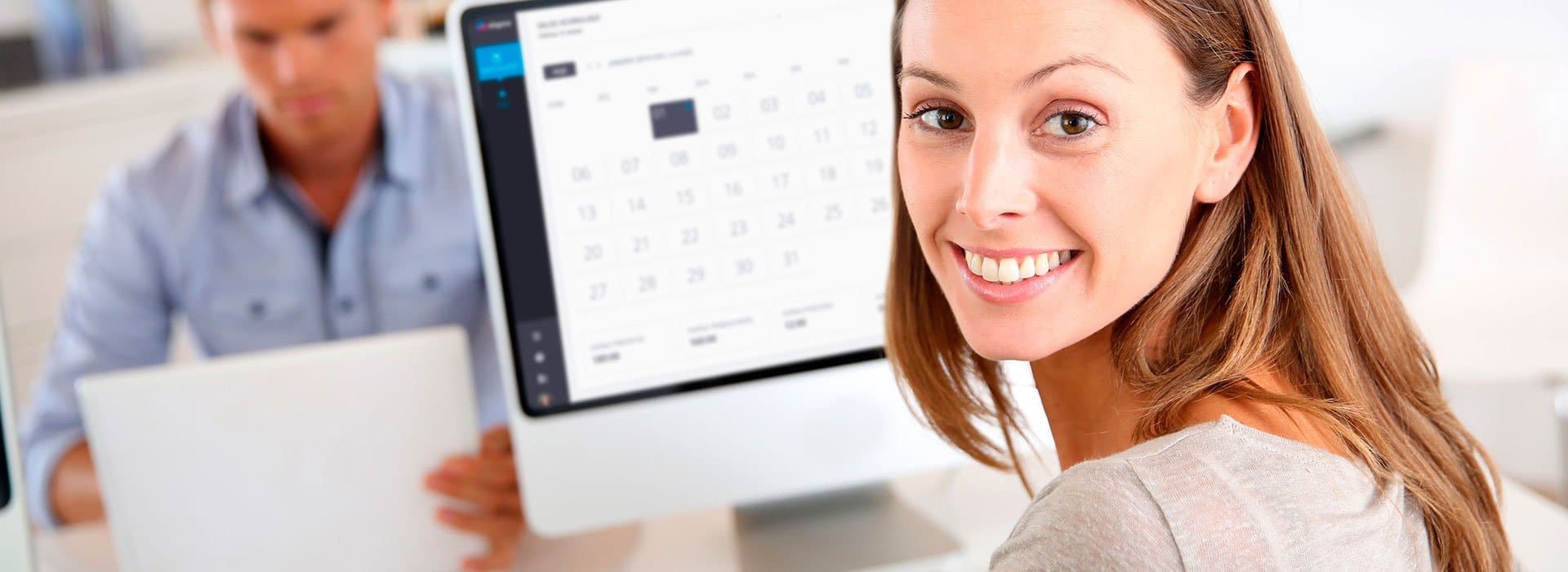 Uma mulher sorrindo com uma tela de computador ao fundo