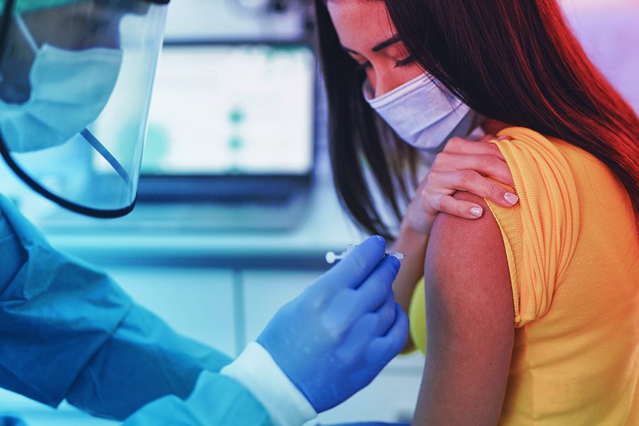 Profissional de enfermagem aplicando a vacina contra a covid-19 no braço de uma mulher